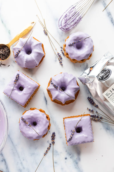 Several black lavender bundt cakes with purple icing on marble counter top.