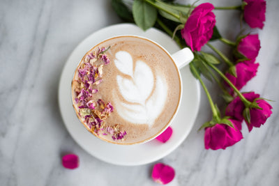 Strawberry Turmeric Lover's Leap Latte with rosetta latte art garnished with roses and a bouquet of roses beside the cup.