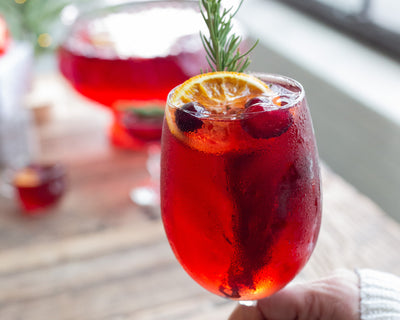 Wine glass filled with Merry Maker's Spritz with cranberry, orange wheel and rosemary garnish.