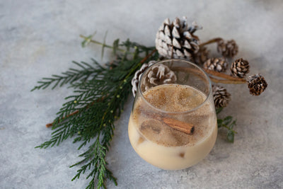 Glass of Ho-Ho-Hojichata with cinnamon stick garnish surrounded by pinecones and tree garland.