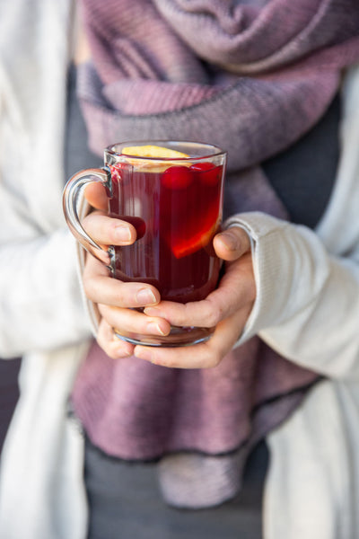 Person holding a glass toddy cup of mulled Merry Maker's punch.