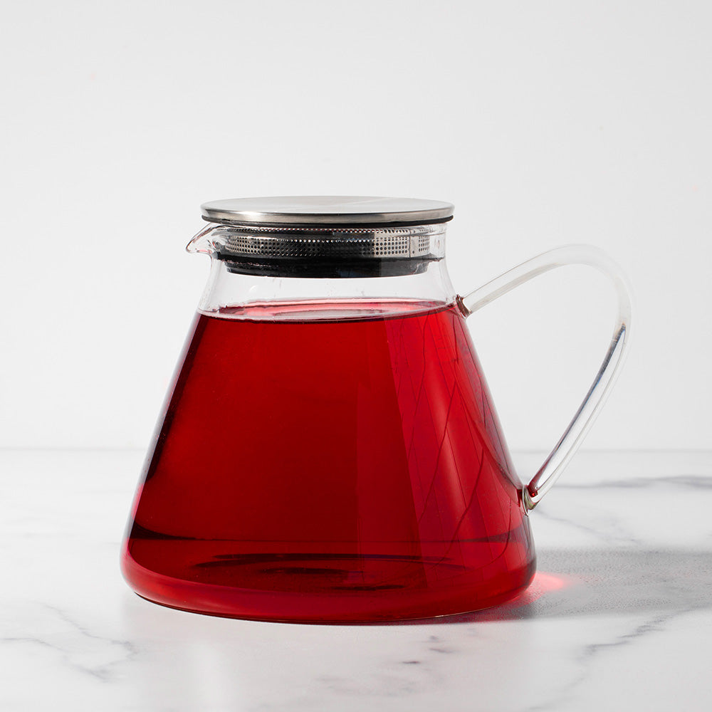 Glass pitcher with silver lid filled with red tea.