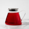 Glass pitcher with silver lid filled with red tea.