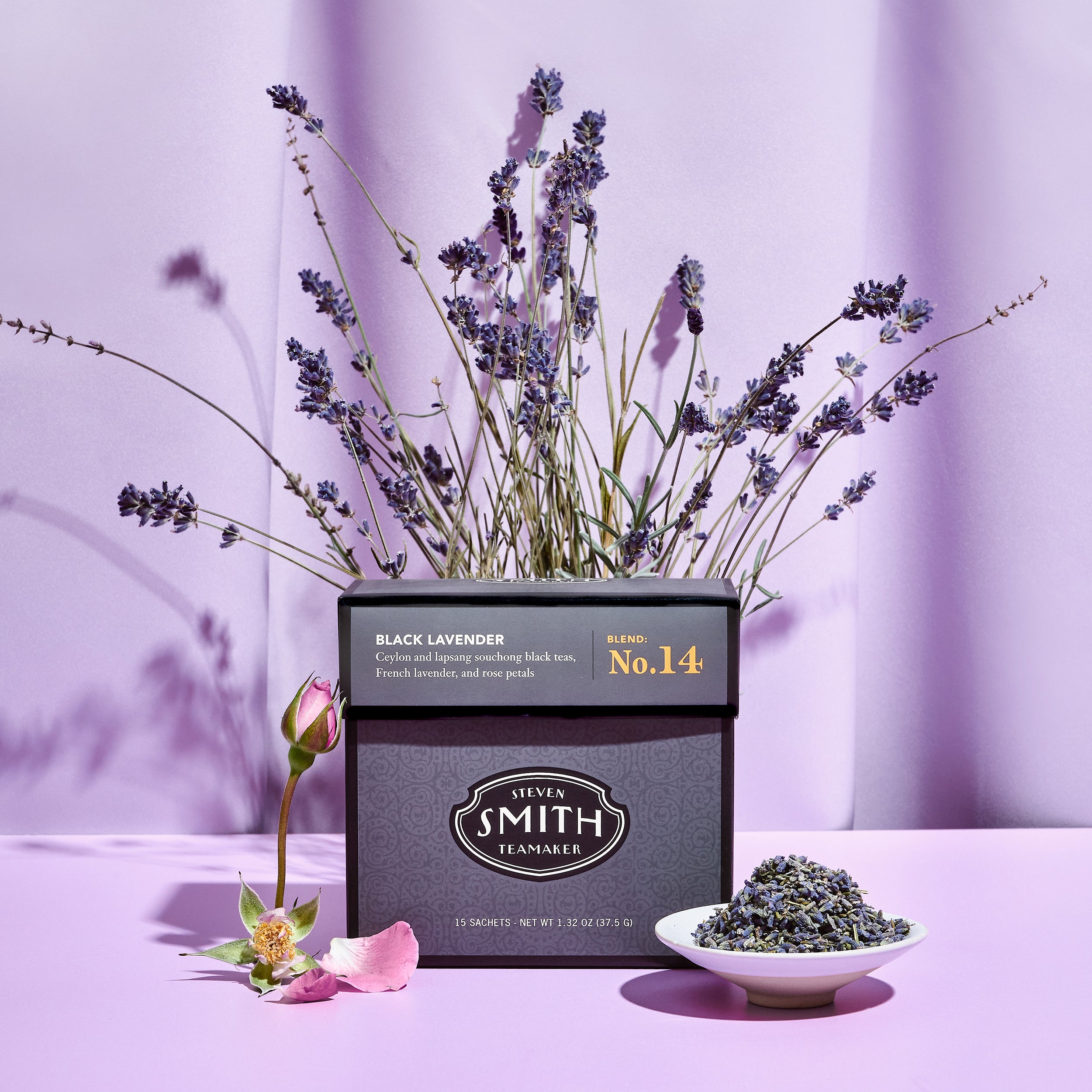 Black box of Black Lavender tea with purple background, rose petals and a pile of lavender.