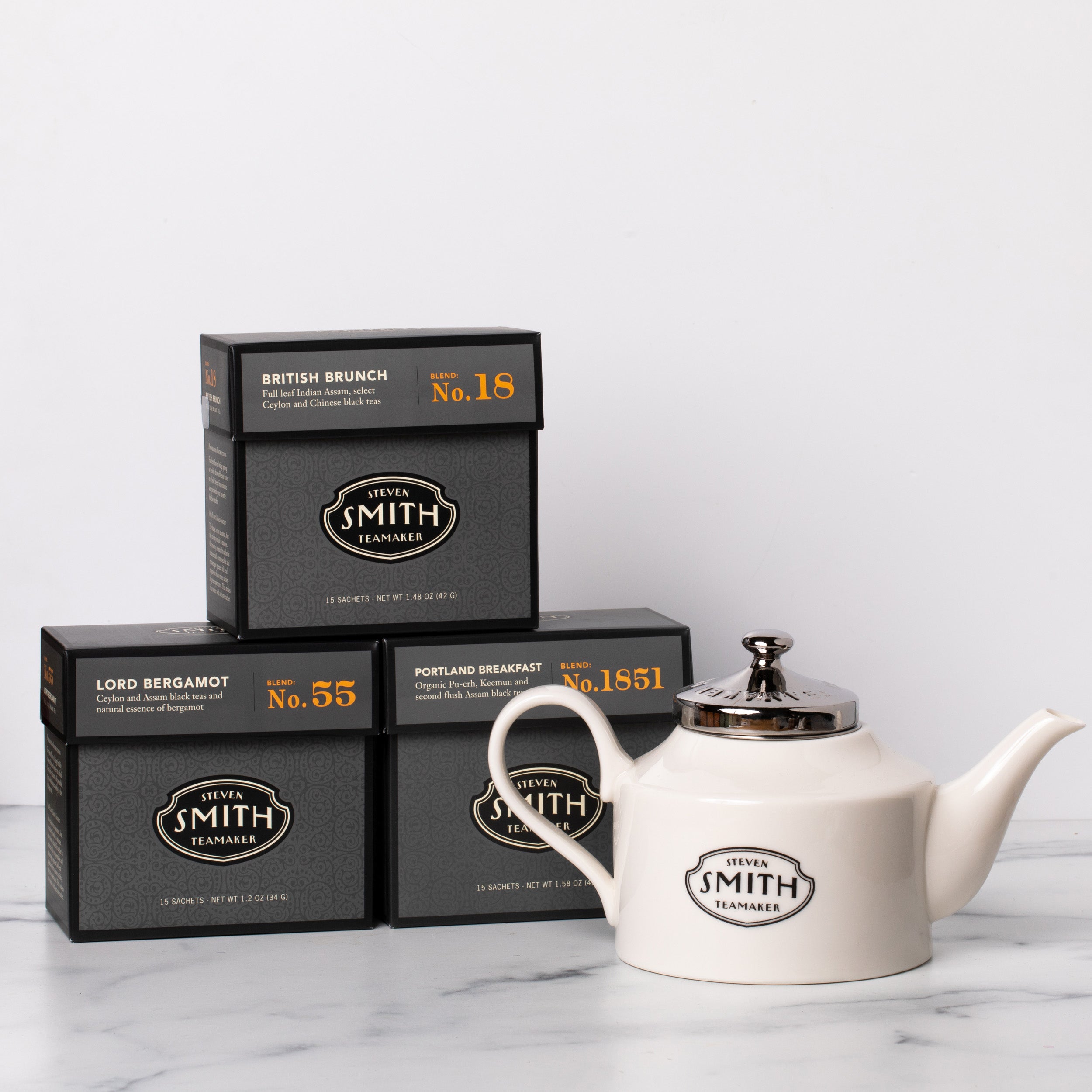 Three cartons of black tea with a white porcelain teapot.