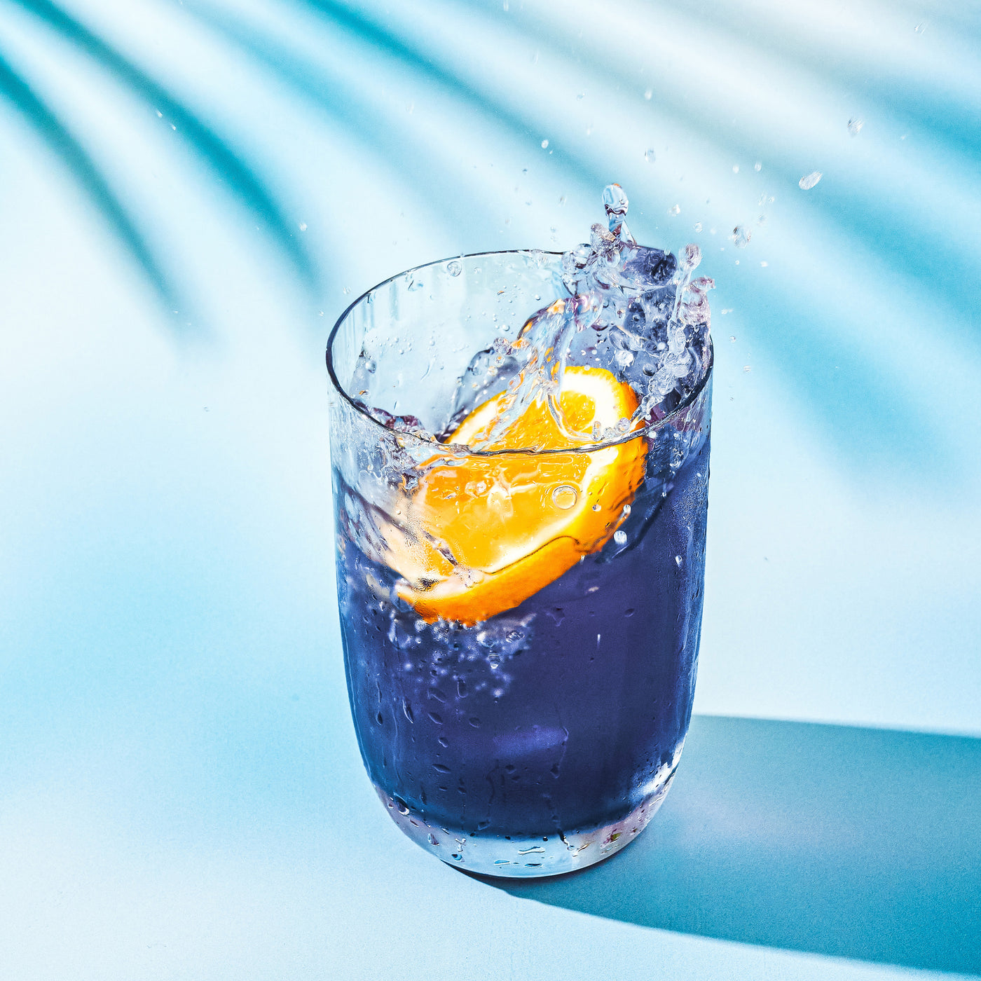 Glass of blue colored Blackberry Jasmine Iced Tea with an orange slice splashing into the glass.