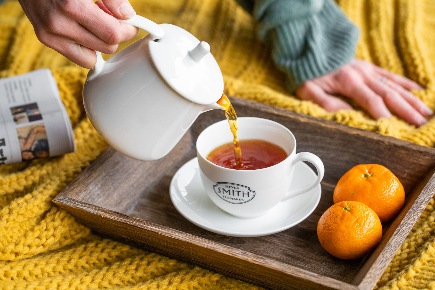 White teapot pouring black tea into Smith Teamaker teacup on wooden tray with tangerines.