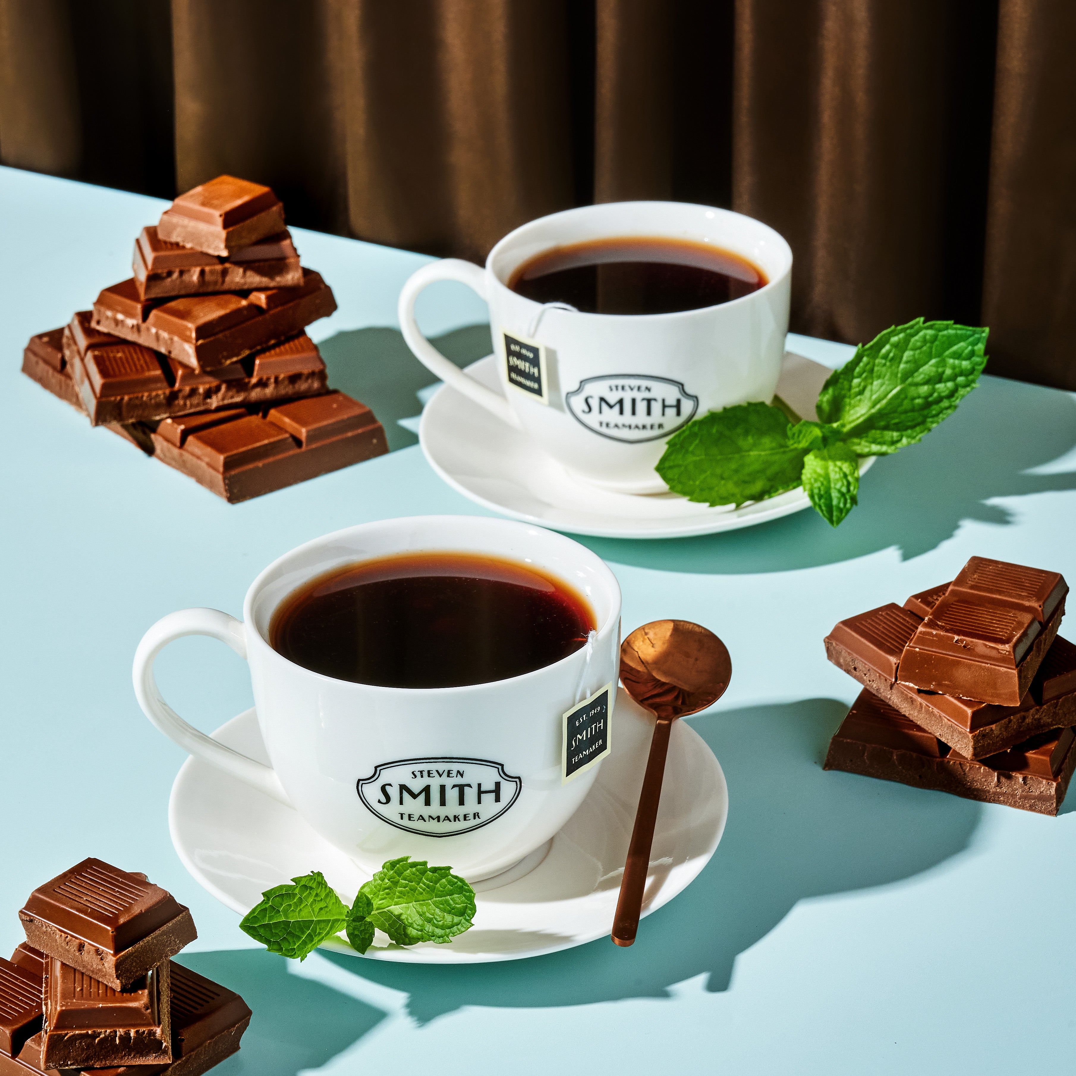 Two Smith branded teacups filled with Chocolate Peppermint Pu-erh brewed tea garnished with fresh mint.
