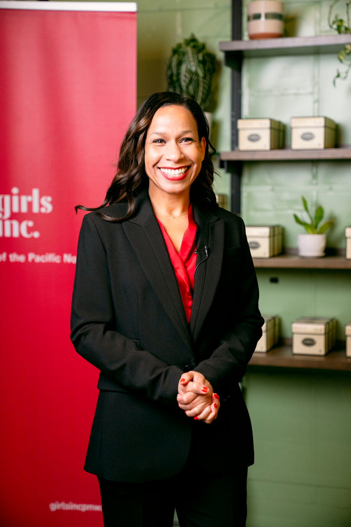 Girls Inc PNW CEO, Cyreena Boston Ashby, standing proudly in front of a red Girls Inc poster.
