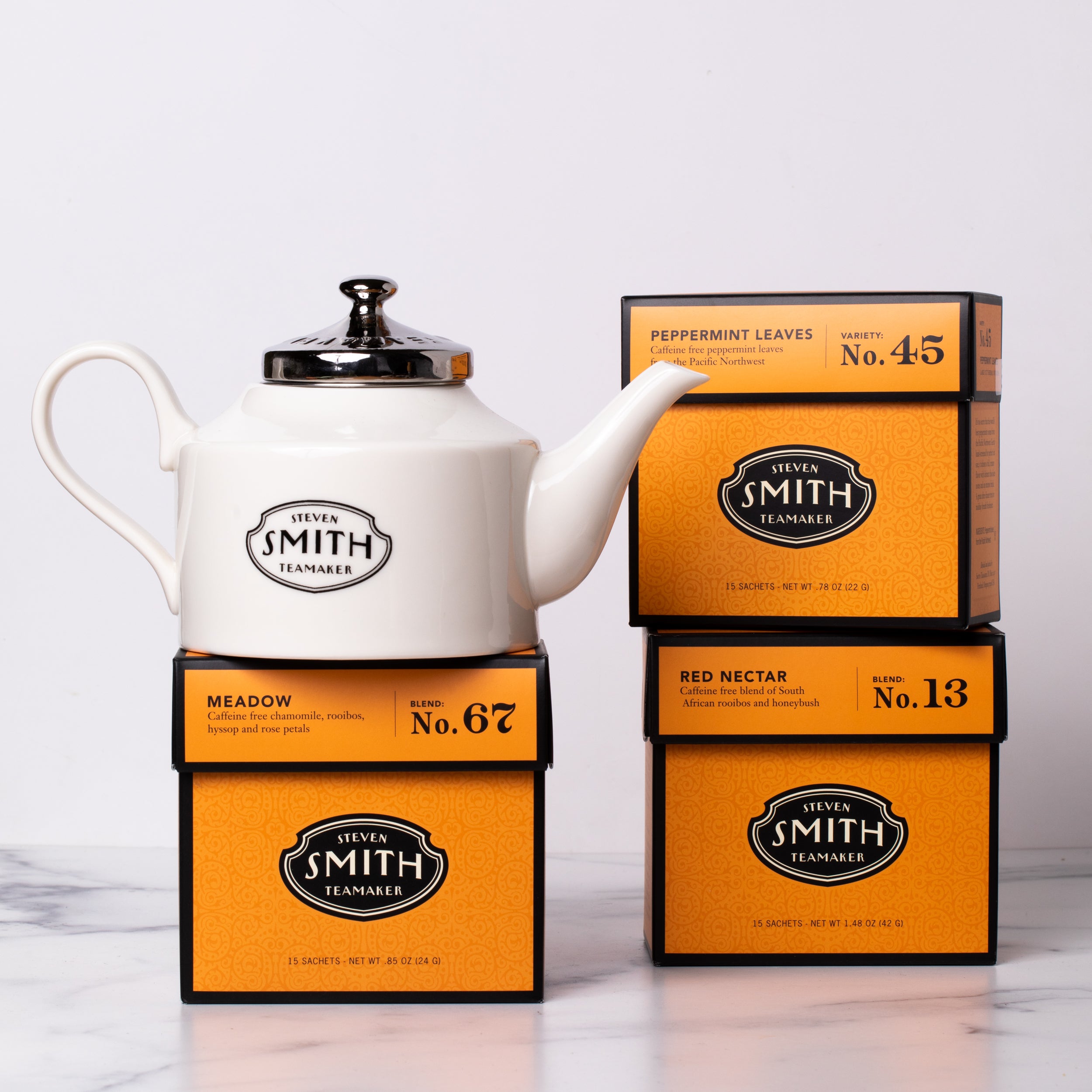 Three orange cartons of herbal tea with a white porcelain teapot.