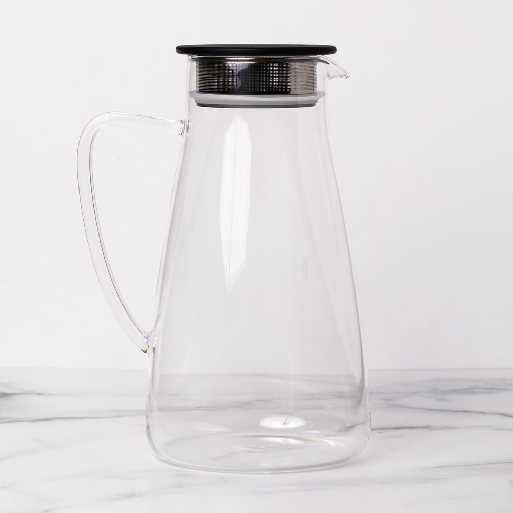 Empty glass pitcher with black lid on marble background.