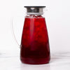 Glass pitcher with black lid filled with red iced tea on marble background.