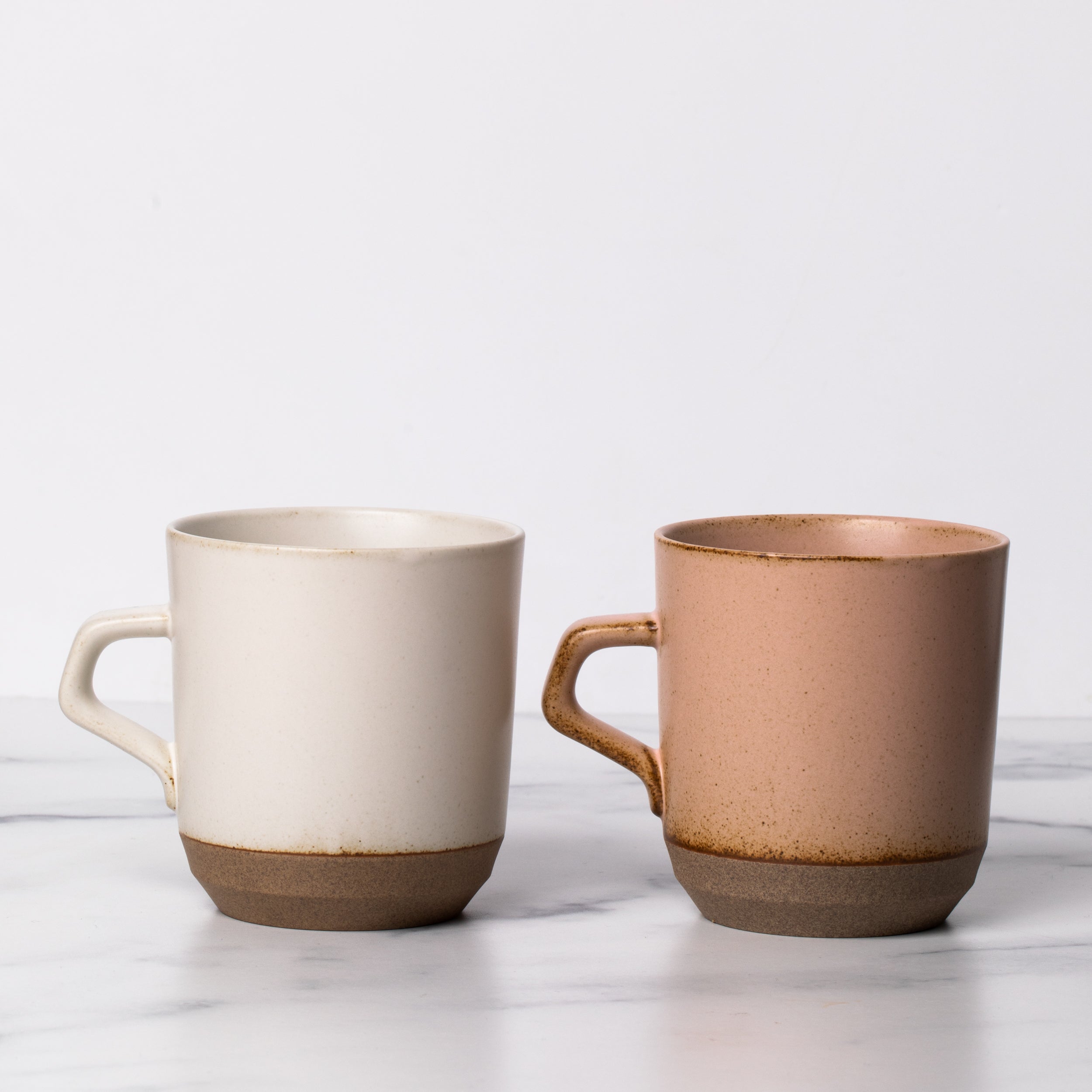 One white ceramic mug with a handle next to a pink ceramic mug with a handle.