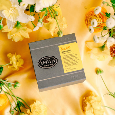 Box of Marigold on a gold cloth surrounded by yellow flowers.