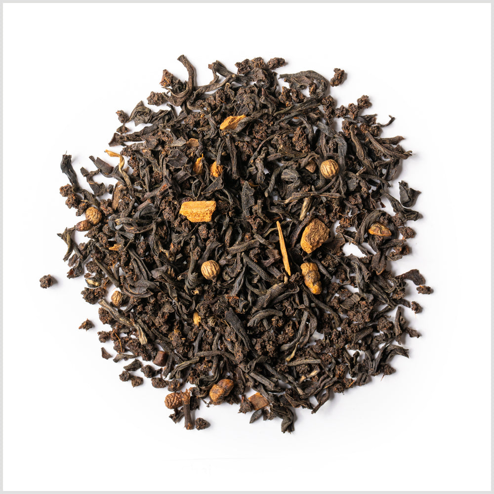 A circular pile of black tea with pieces of dried black pepper, ginger, cassia and ginger.