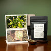Post cards with photos of tea fields and jasmine buds next to black bag with white label on wood table.