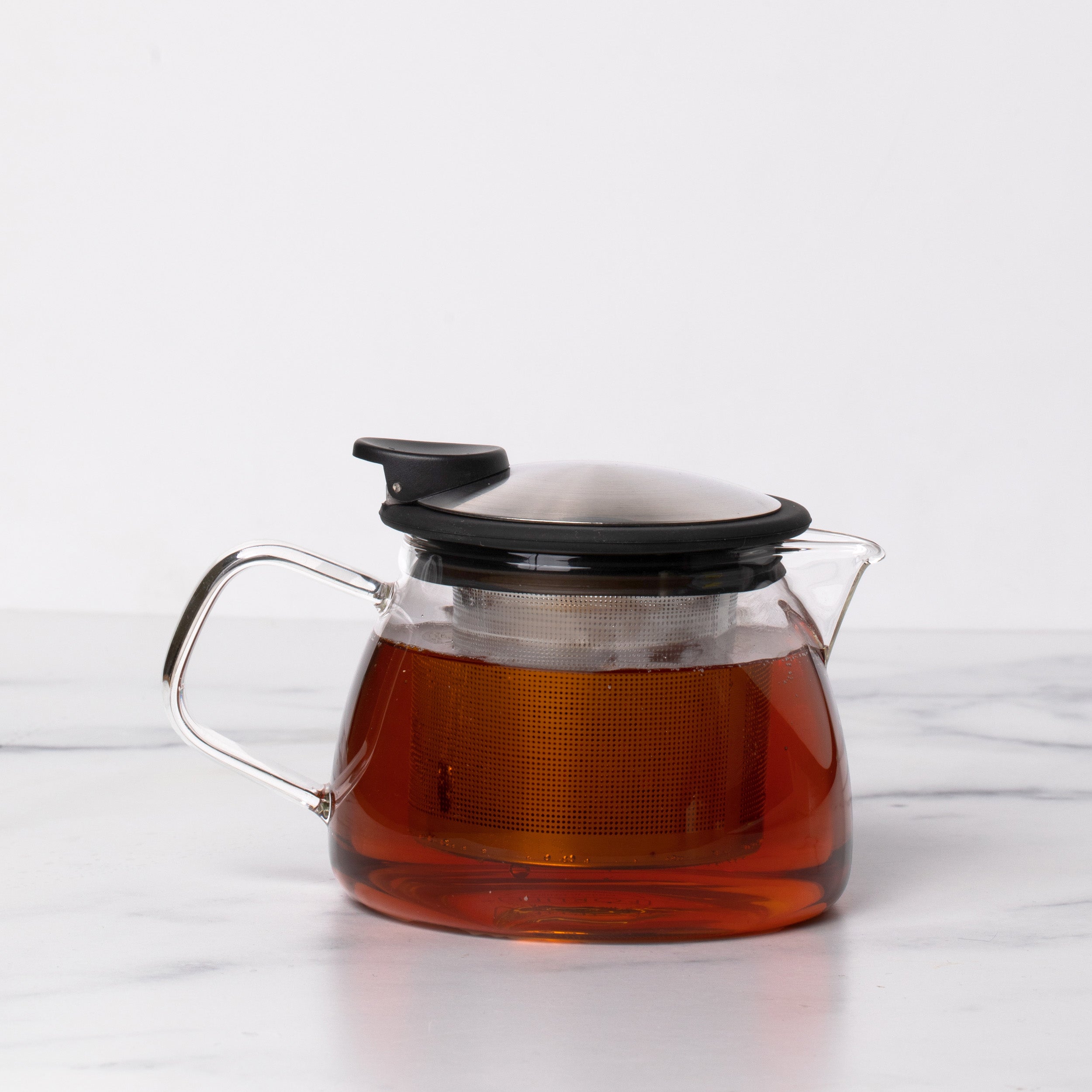 Glass teapot with stainless steel and black lid with spout and handle filled with amber colored tea.