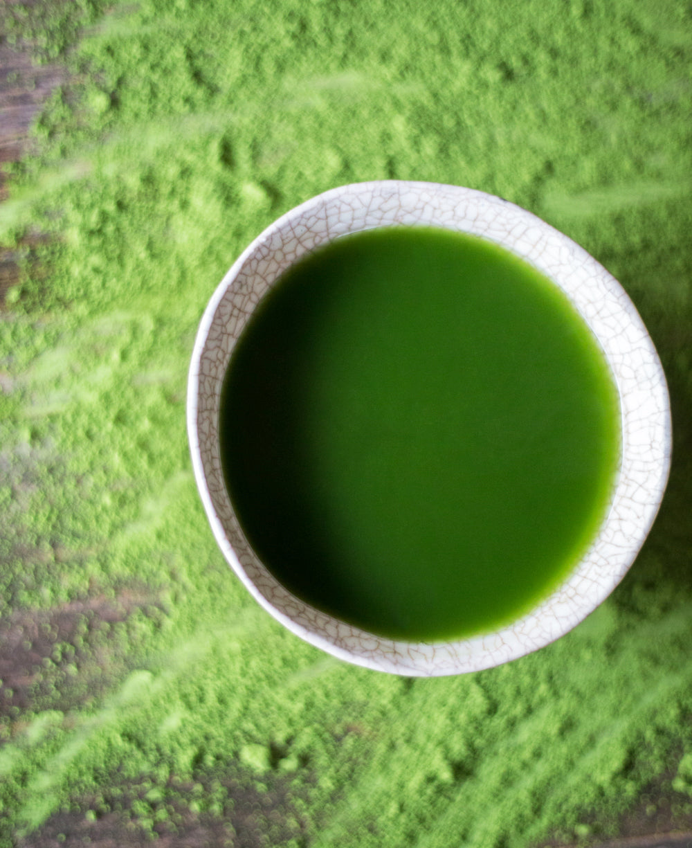 Ceramic bowl of ceremonial matcha on a counter top with matcha powder scattered.