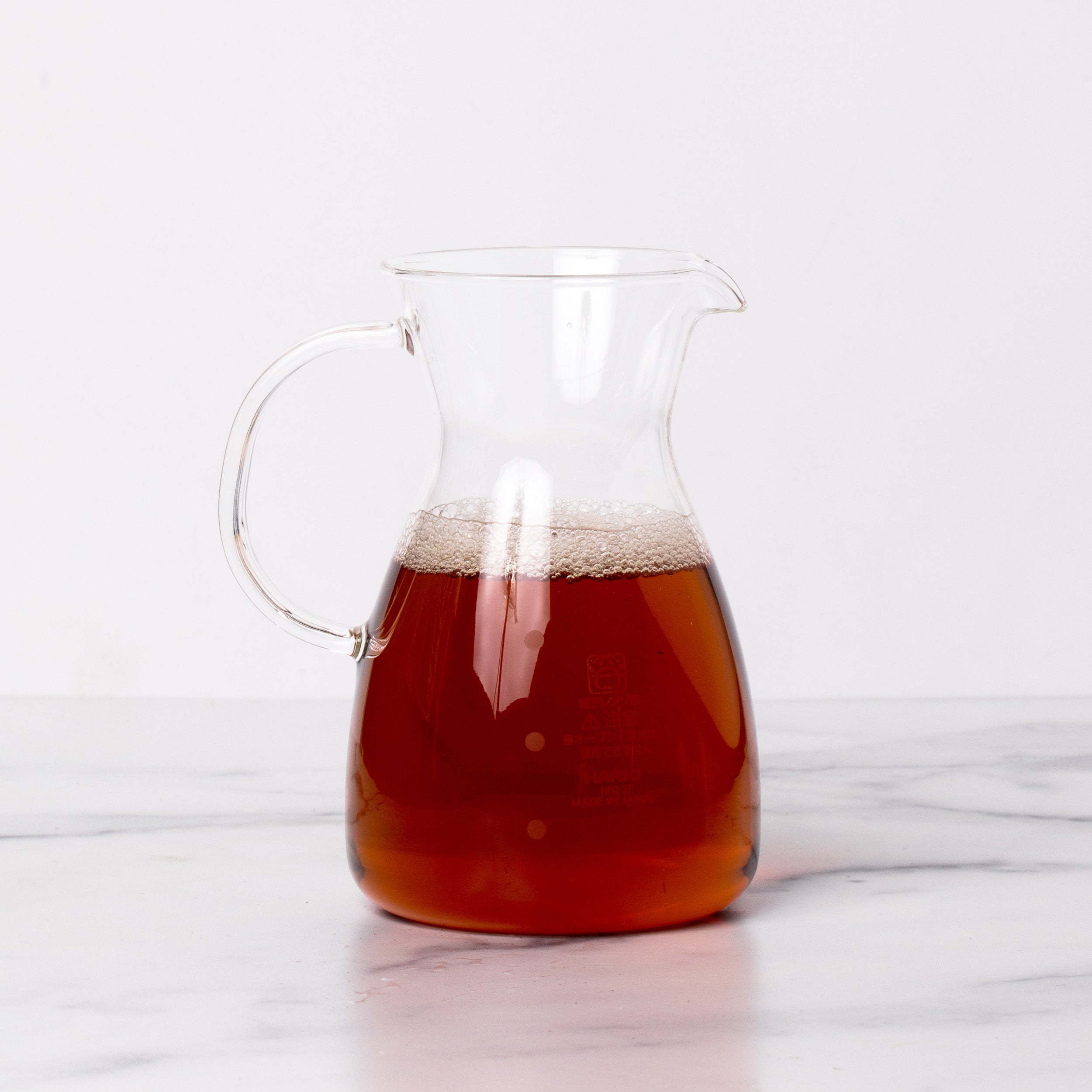 Glass decanter filled with amber tea liquid on a marble background.