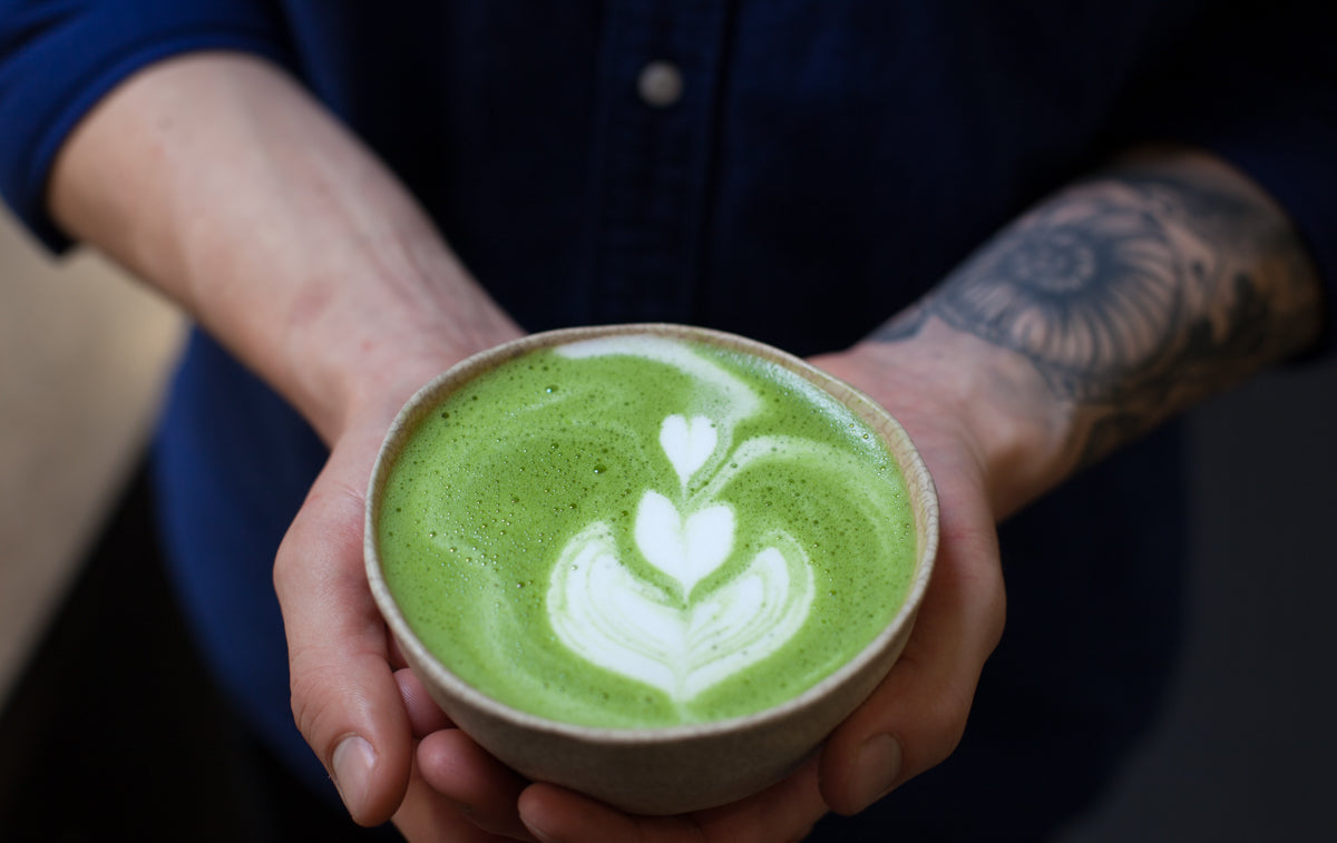 Hands holding a bowl filled with matcha latte with rosette latte art.