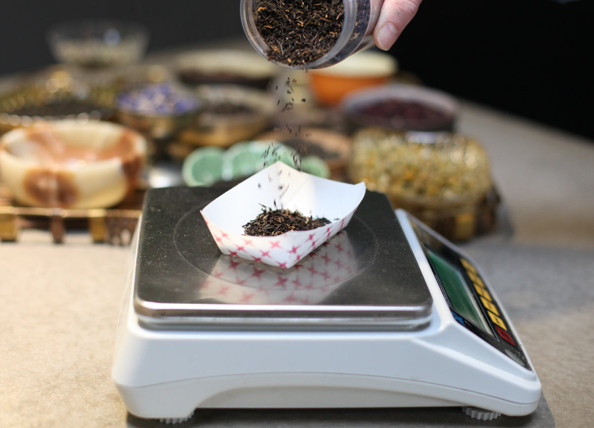 Hand pouring loose tea from a sample jar into a small french fry tray to weigh loose tea.