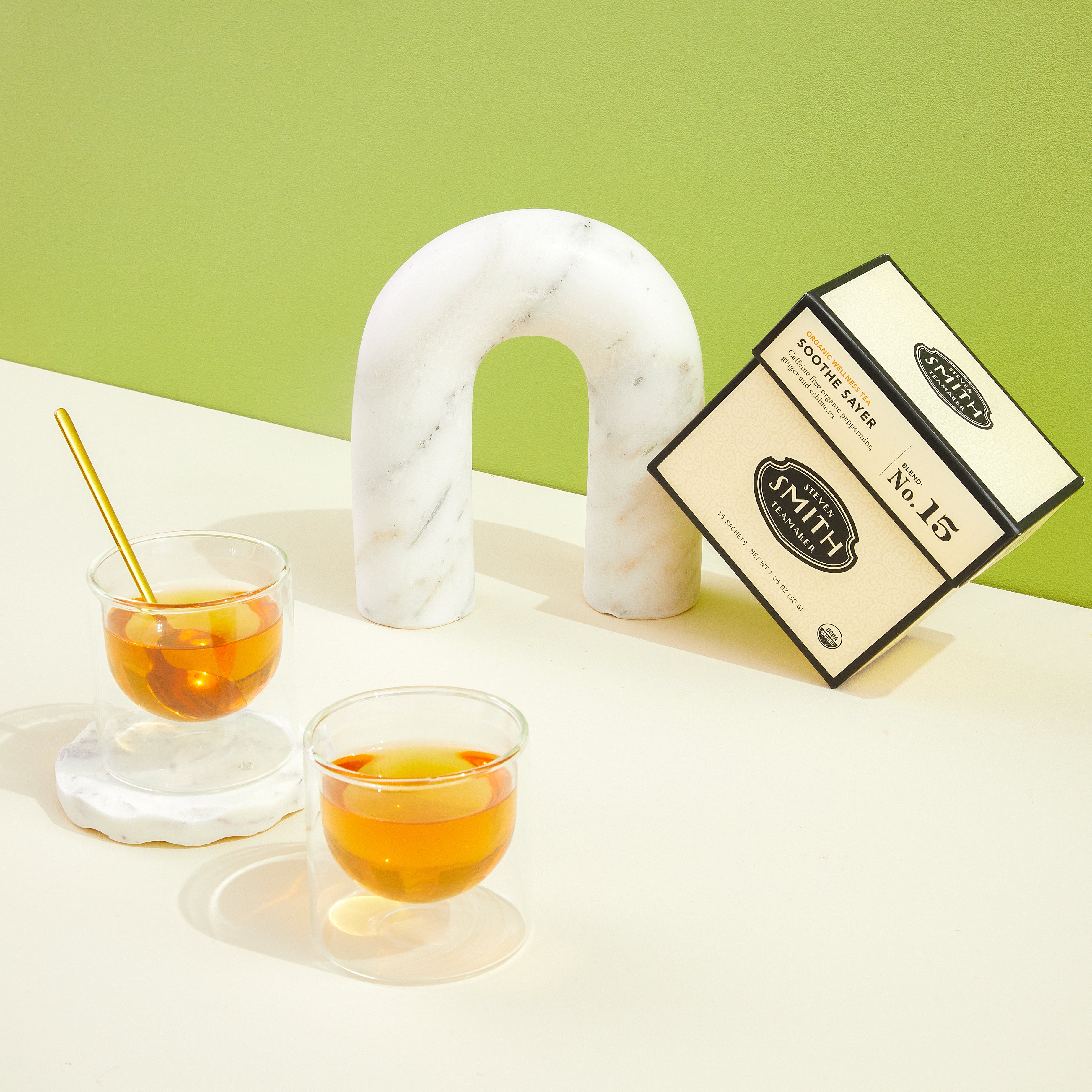 Cream carton of Soothe Sayer wellness tea with two glass cups on a table.