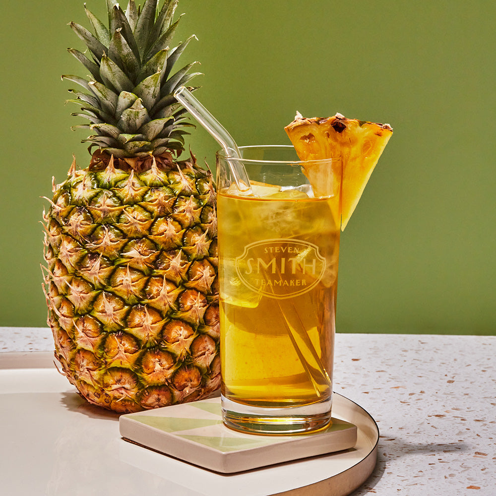 Full glass of yellow iced tea on a table with pineapple wedge as garnish with a straw.