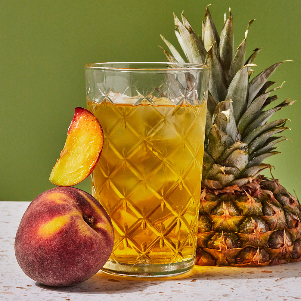 Full glass of yellow Pineapple Green Iced Tea with fresh cut tropical fruit.