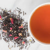 Pile of full leaf black tea with rose petals and lavender next to cup of tea.