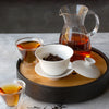 Glass decanter filled with amber tea liquid on a wooden tray.