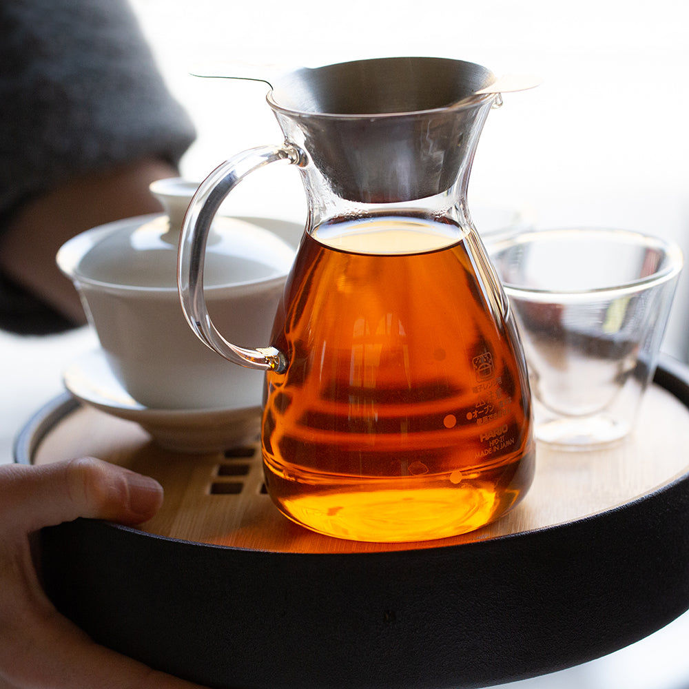 Glass decanter filled with amber tea liquid on a wooden tray.
