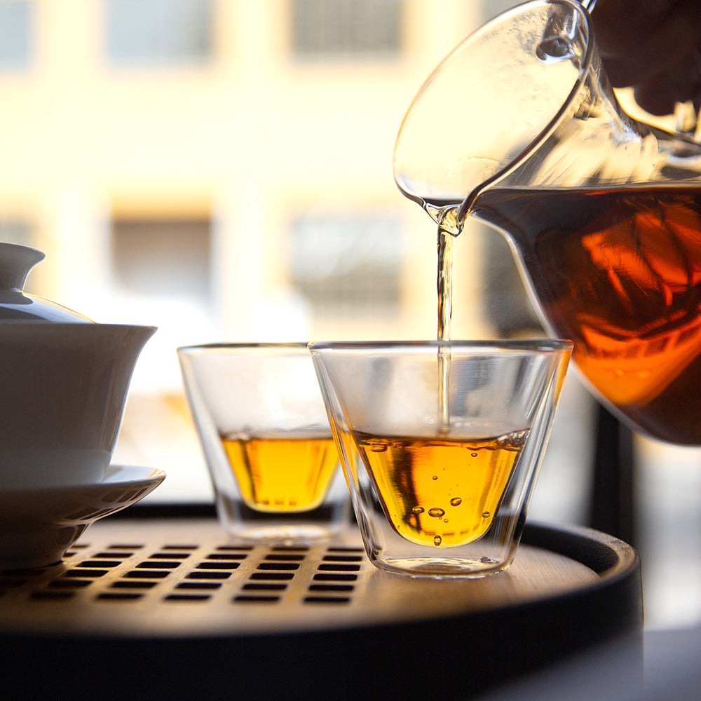 Glass decanter filled with amber colored tea pouring into two glass cups.