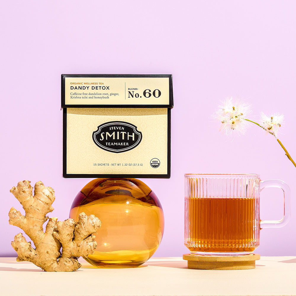 Cream box of Dandy Detox with fresh ginger and a cup of tea on table.
