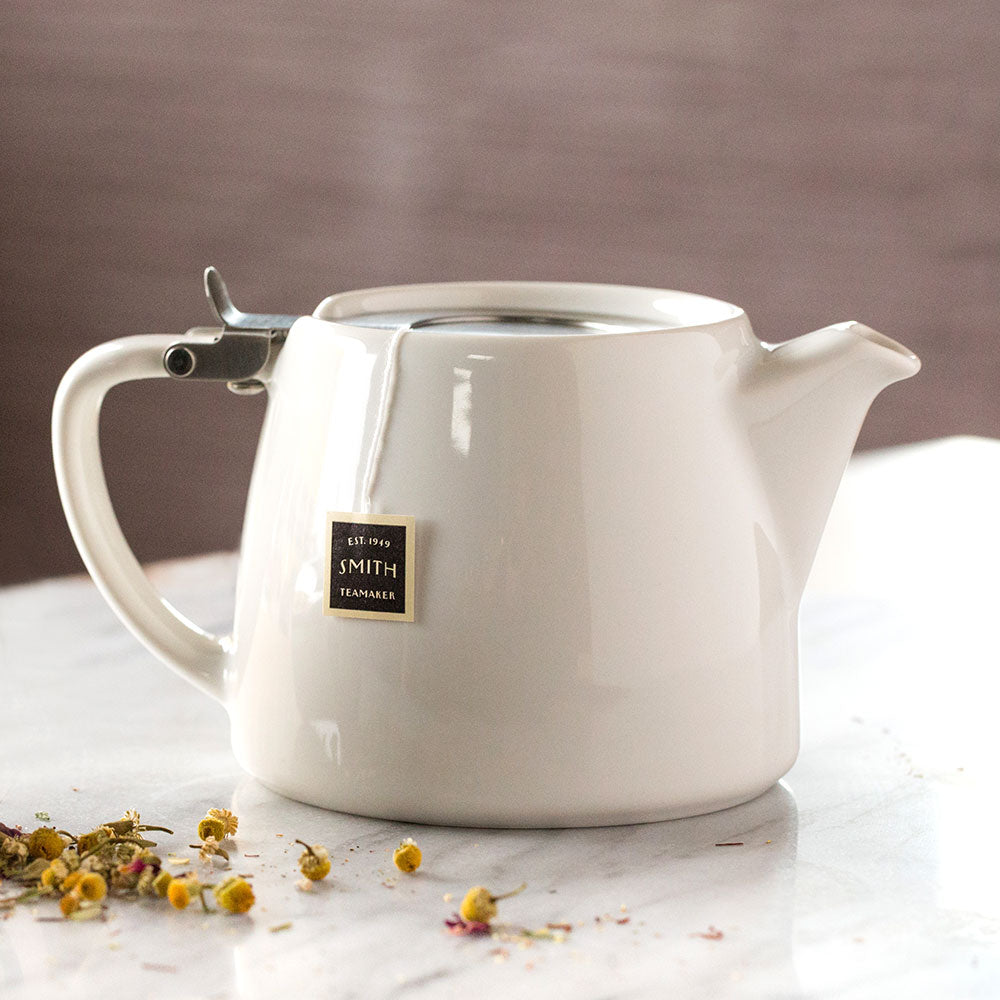 White ceramic teapot with stainless steel top on a marble table.