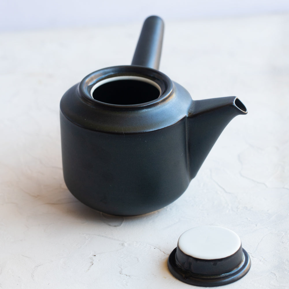 Black lidded teapot with spout and long handle.