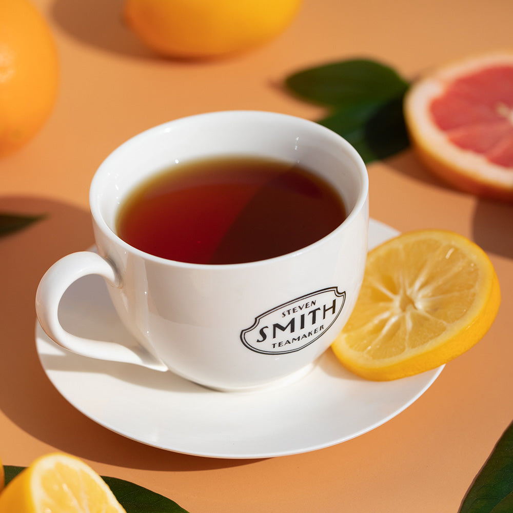 White porcelain teacup with Smith Teamaker logo on a saucer with a slice of lemon. 
