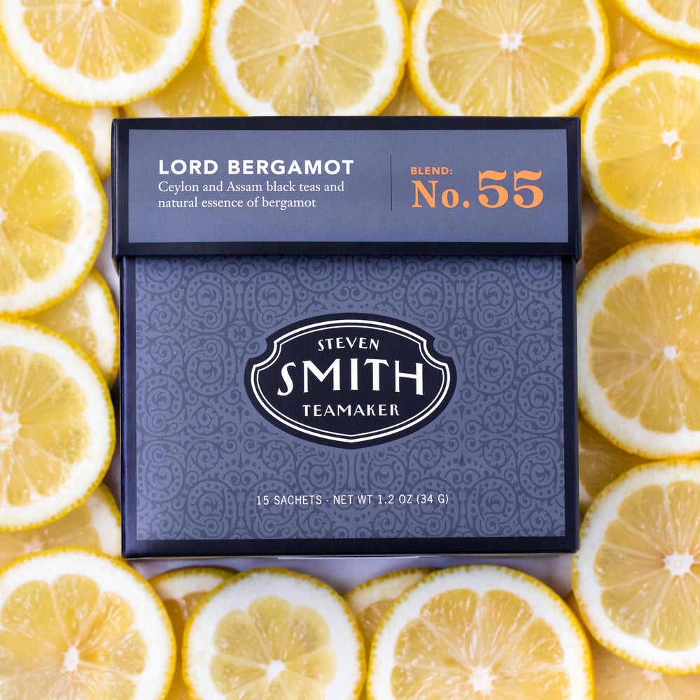 Grey carton of Lord Bergamot Black Tea surrounded by fresh cut slices of lemon. 