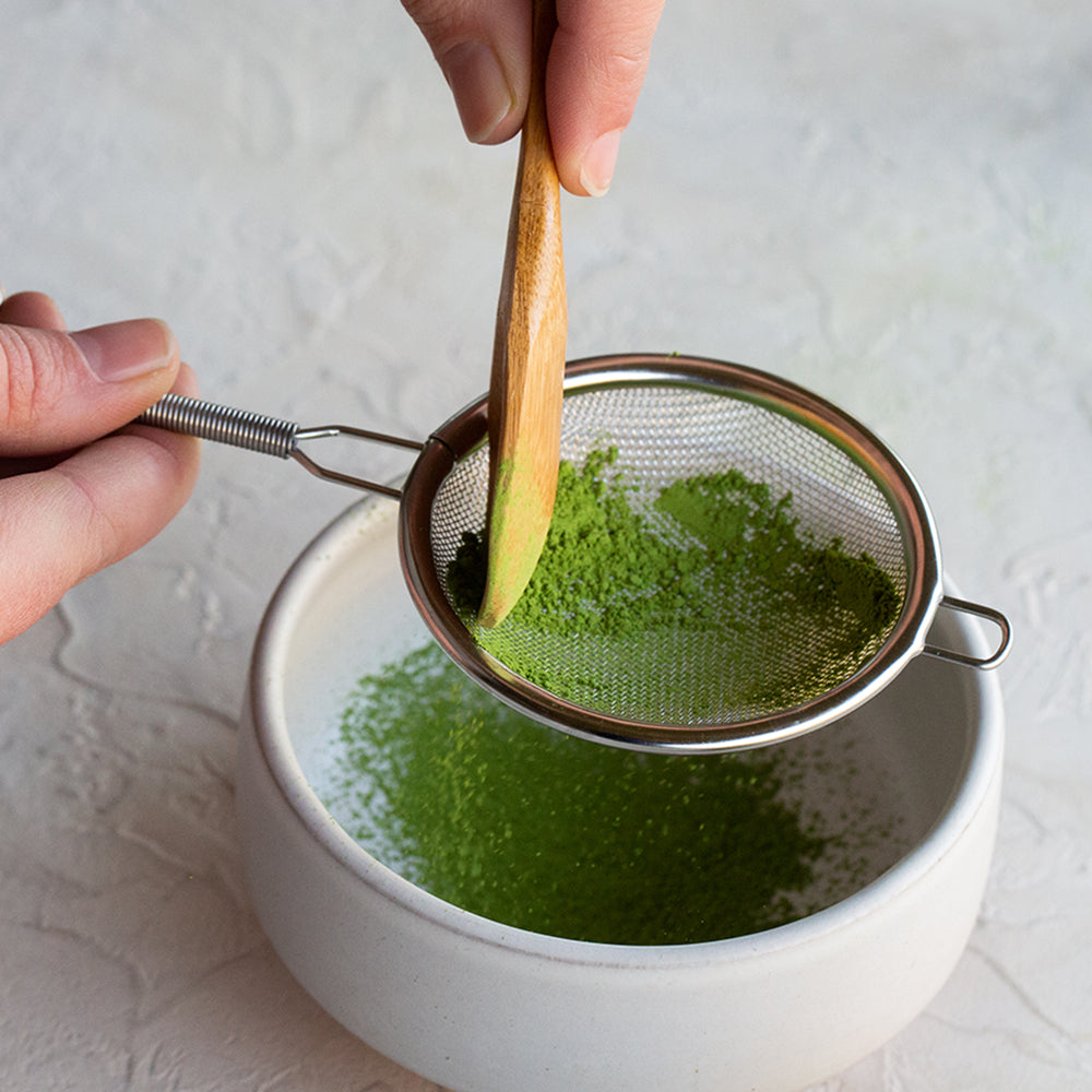 Hand sifting matcha through silver netted sifter.