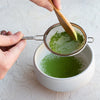 Hand sifting matcha through silver netted sifter.
