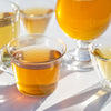 Five glass cups filled with golden yellow tea on a white background.