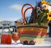 Pitcher filled with brown iced tea next to picnic basket filled with flowers.