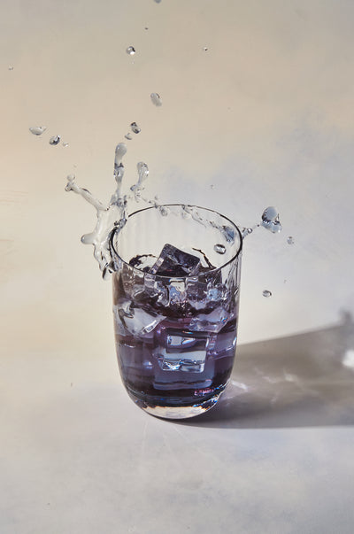 Glass of blue iced tea with ice cube thrown in to create splash.