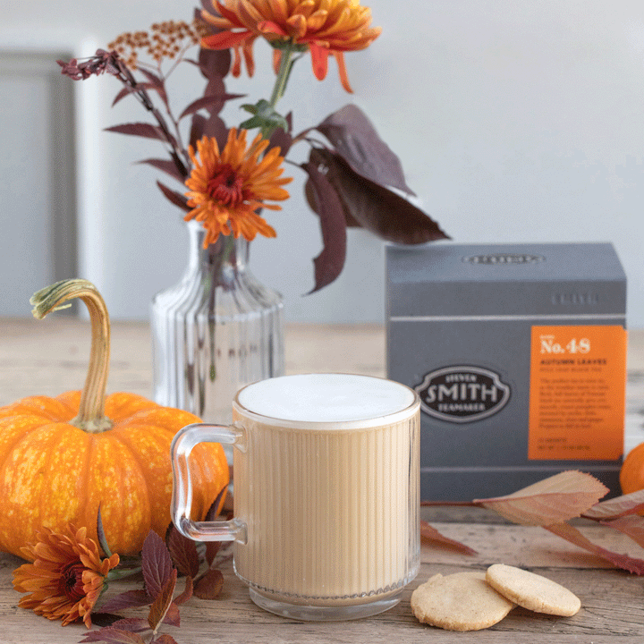 Harvest Moon Latte in glass mug beside pumpkin, sugar cookies and a box of Autumn Leaves tea.