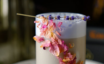Up close of a glass with iced Black Lavender vanilla latte with purple cold foam, lavender garnish and rose garnish.