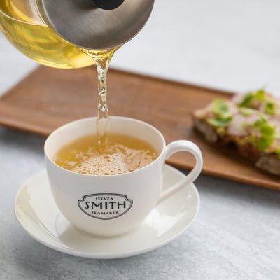 Glass teapot pouring green tea into Smith branded teacup.