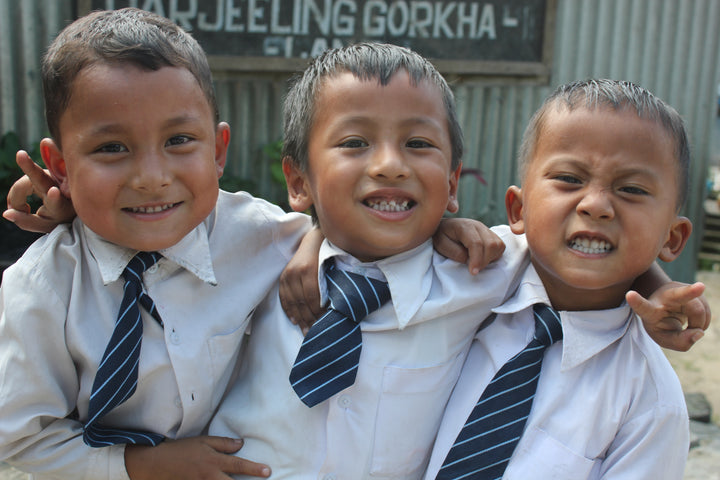 Three school boys with big smiles and wearing blue uniforms.