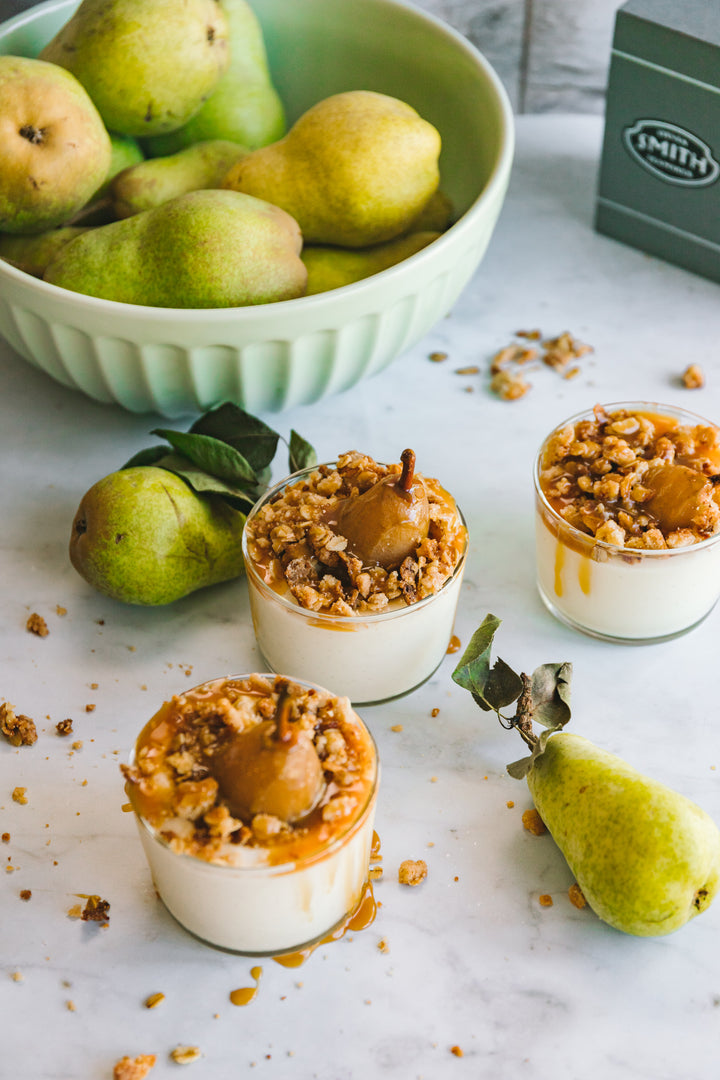Three cups of tea poached pear cheesecakes with bowl of pears in background.