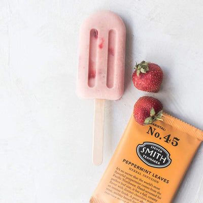 Pink Peppermint Strawberry Creamsicle on marble counter with two strawberries and orange wrapped sachet of peppermint tea.
