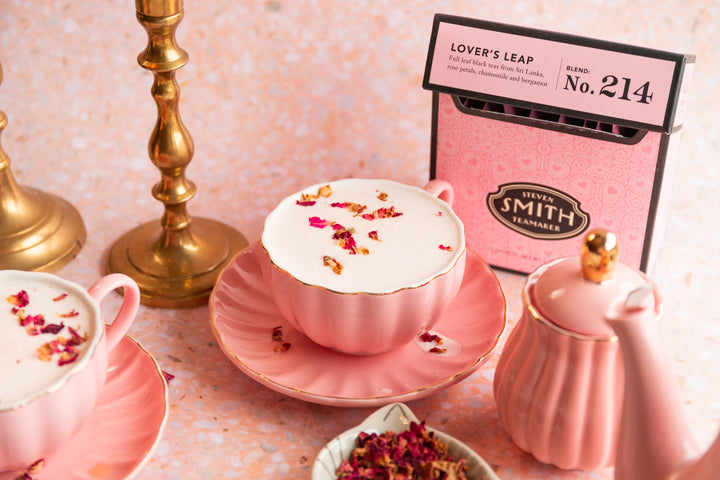 Pink background with pink teacup of Lover's Leap Glitter Latte and a pink box of Lover's Leap tea.