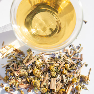 Glass teacup of brewed Lullaby beside pile of loose leaf Lullaby wellness tea.